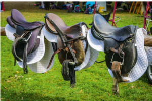 Drei unterschiedliche Sättel sind auf einer horizontalen Stange abgelegt.